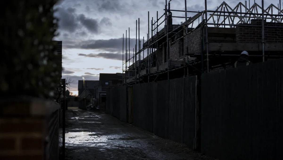 Scaffolding on a part-built brick house at dusk, wet ground reflecting the last of the light.